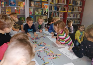 Dzieci przy stoliku kolorują karty pracy